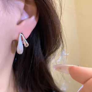 Primo piano di orecchini minimalisti a perno in argento spazzolato a goccia indossati sull'orecchio