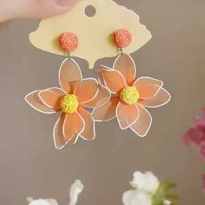 Close-up detail of orange raffia flower earrings with hollow mesh petals in bohemian style