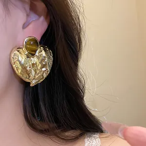 Detailansicht eines goldenen Herz-Ohrrings mit einem eingelegten Tigerauge-Edelstein
