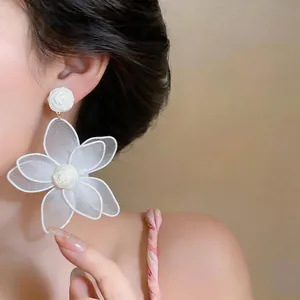 Close-up of large white mesh flower earrings with rose stud detail in bohemian style.