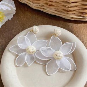 Close-up of white mesh flower earrings with raffia centers for bohemian beach style.