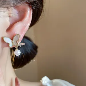 Close-up detail of 14k gold plated butterfly stud earrings featuring zircon and pearl.