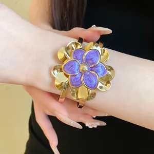 Close-up of a vintage gold cuff bracelet with a large purple enamel double flower detail.
