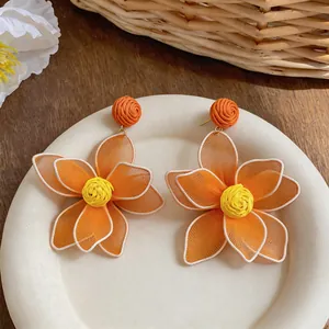Close-up of orange mesh flower earrings with raffia woven detail for a summer beach look