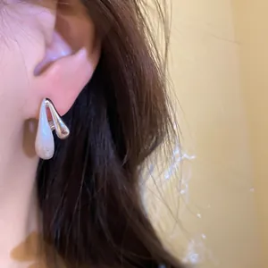 Dettaglio ravvicinato di un orecchino a goccia minimalista in argento spazzolato su modella