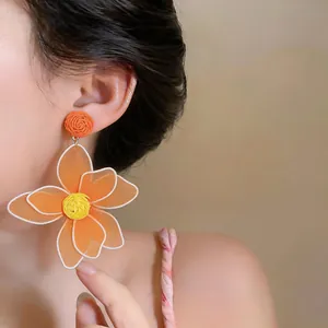 Detailed close-up of a vibrant orange bohemian raffia flower earring worn by a model