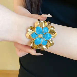 Close-up view of a vintage gold-toned cuff bracelet featuring a blue enamel flower design.