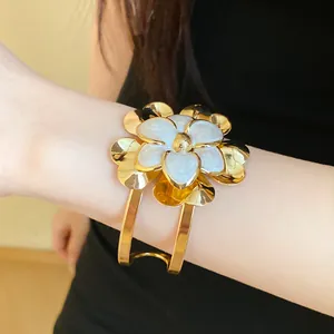 Detailed macro shot of a gold vintage open cuff bracelet with white enamel flower on wrist.