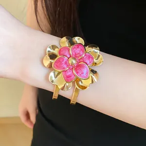 Detail view of a vintage gold metal open bracelet with a pink enamel flower design.