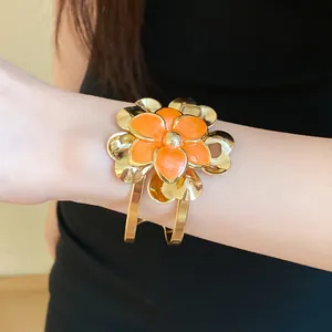 Macro shot of a vintage gold cuff bracelet with an orange enamel double flower design.
