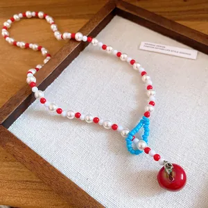Dettaglio del ciondolo a ciliegia rossa e della collana di perle bianche da donna