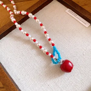Primo piano dettagliato di una collana di perle con mela rossa e perline colorate.