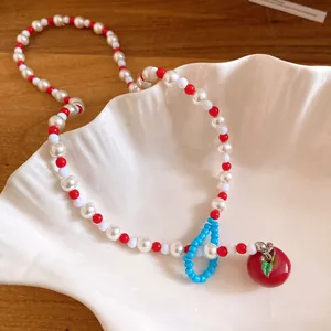 Primo piano di una collana di perle con ciondolo a mela rossa in una conchiglia bianca.