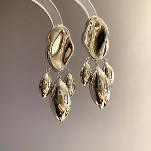 Close-up of irregular distorted silver-finish geometric pendant earrings with high shine.