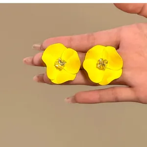 Close-up view of bright yellow flower earrings with a square yellow rhinestone inlay