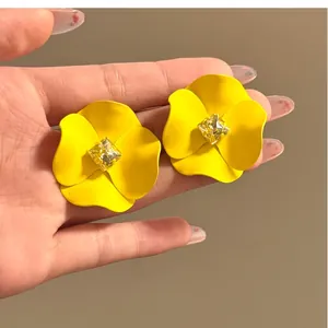 Close-up of yellow flower stud earrings with center square yellow gemstone in hand.