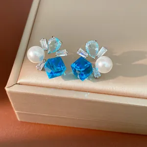 Elegante Ohrstecker mit leuchtend blauen Kristallen und glänzenden weißen Perlen im Detail