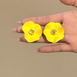 Close-up of vibrant yellow spray-painted flower stud earrings with a central yellow crystal.