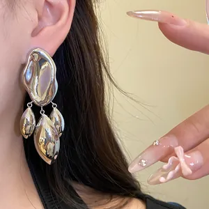 Close-up of silver-toned glossy irregular geometric earrings worn on an Asian ear.