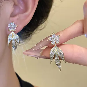 Close-up detail showing 14k gold plated zircon flower and leaf tassel earrings on model