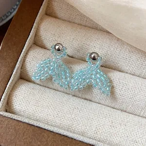 Close-up detail of light blue beaded fishtail earrings inside a cream jewelry box