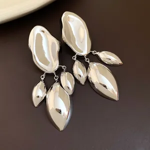 Macro detail of shiny silver irregular geometric earrings with three leaf pendants on brown base