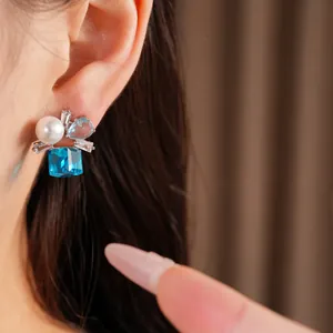 Nahaufnahme eines silbernen Steckohrrings mit blauem Zirkon und einer weißen Perle