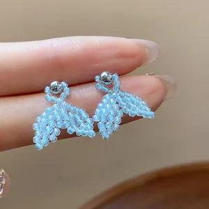 Macro detail of light blue beaded fishtail earrings with silver studs on fingers