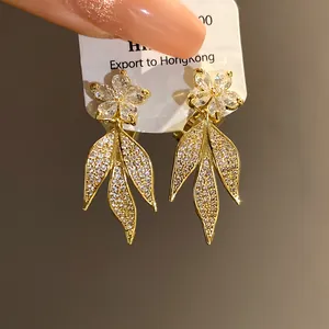 Macro detail of 14k gold plated clip-on earrings with zircon flowers and leaf tassels