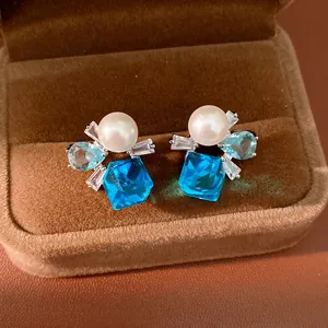 Detailansicht eleganter Silberohrringe mit blauen Edelsteinen und weißen Perlen.