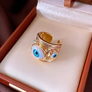 Exaggerated gold-tone open ring featuring blue resin evil eye designs in a luxury box