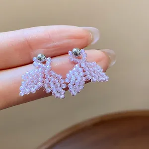 Detailed macro view of exquisite handmade purple seed bead fishtail stud earrings on finger