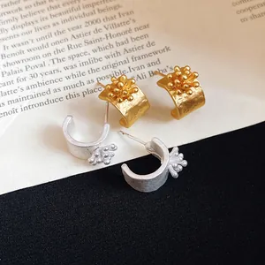 Close-up of gold and silver vintage flower C-shaped stud earrings with matte texture