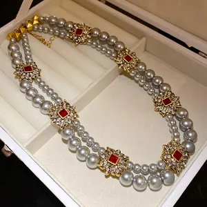 Detail of double-layer grey pearl necklace with gold flower and red stone accents