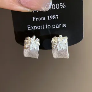 Detail view of intricate silver floral C-shaped earrings with matte textured finish
