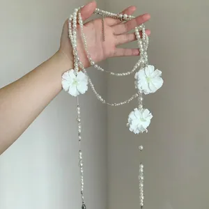 Dettaglio della collana lunga di perle multistrato con eleganti fiori di camelia.
