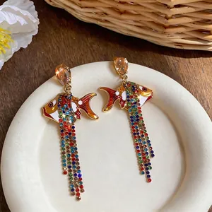 Boucles d'oreilles pendantes poisson en émail et strass colorés sur plateau blanc
