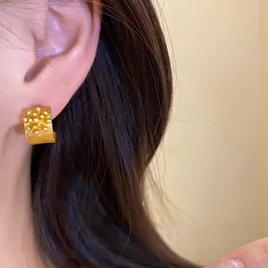 Close-up of vintage gold C-shaped earrings with floral texture on a model's ear