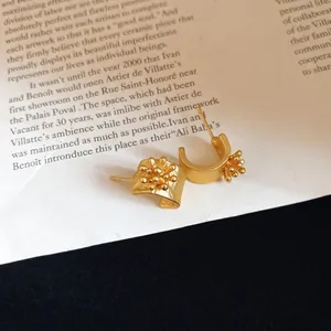 Vintage gold C-shaped stud earrings with intricate flower detailing on magazine background