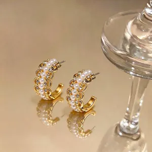 Elegant C-shaped gold hoop earrings with pearls and rhinestones on a warm gold surface