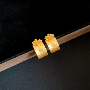 Close-up of elegant gold matte C-shaped earrings with floral bud design on velvet