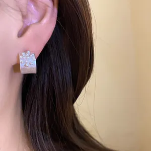 Detailed macro view of vintage silver C-shaped earrings with textured flower motif on ear