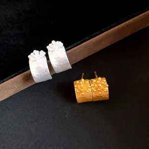Macro detail of textured retro C-shaped stud earrings in matte gold and silver finishes