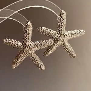 Elegant silver starfish stud earrings with realistic texture on a soft warm background