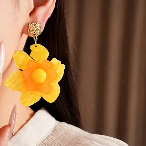 Elegant yellow resin flower drop earrings worn by a model in a luxury setting