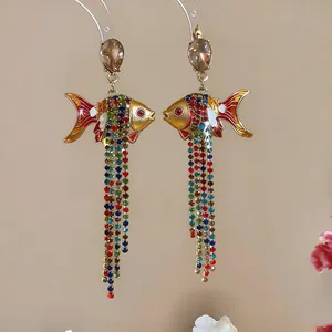 Vue détaillée de boucles d'oreilles poisson dorées avec glands en strass colorés et émail