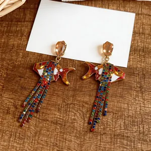 Détail de boucles d'oreilles poisson dorées avec pompons en strass multicolores