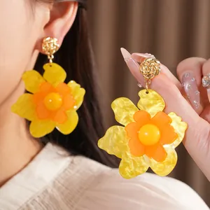 Detailed view of yellow resin flower earrings with gold rose studs on an Asian model.