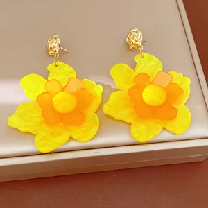 Macro detail of vibrant yellow and orange resin flower earrings on a luxury display box