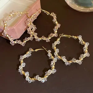 Close-up of gold-tone twisted hoop earrings featuring clear faceted beads and spiral design
